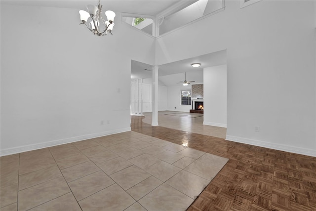 empty room featuring ceiling fan with notable chandelier, high vaulted ceiling, decorative columns, a large fireplace, and light tile patterned floors