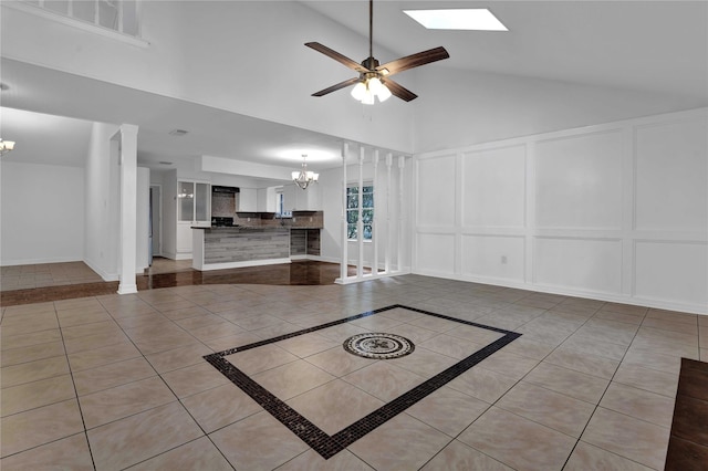 unfurnished living room featuring light tile patterned floors, ceiling fan with notable chandelier, and vaulted ceiling with skylight