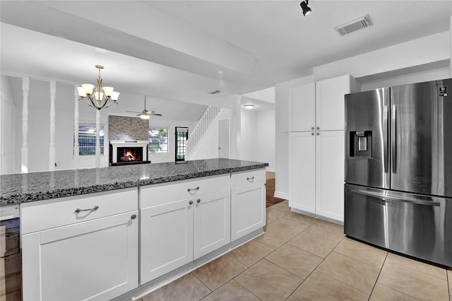 kitchen with a fireplace, dark stone countertops, white cabinets, light tile patterned floors, and stainless steel refrigerator with ice dispenser