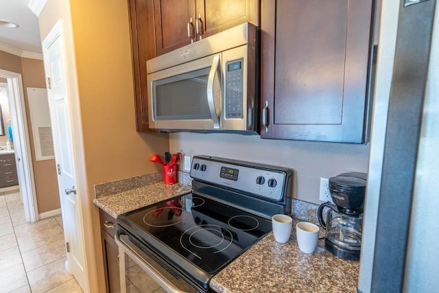 kitchen featuring dark stone countertops, light tile patterned floors, ornamental molding, and appliances with stainless steel finishes