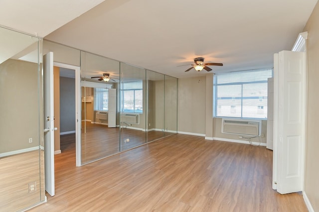 unfurnished bedroom featuring a wall mounted air conditioner, hardwood / wood-style floors, multiple windows, and ceiling fan