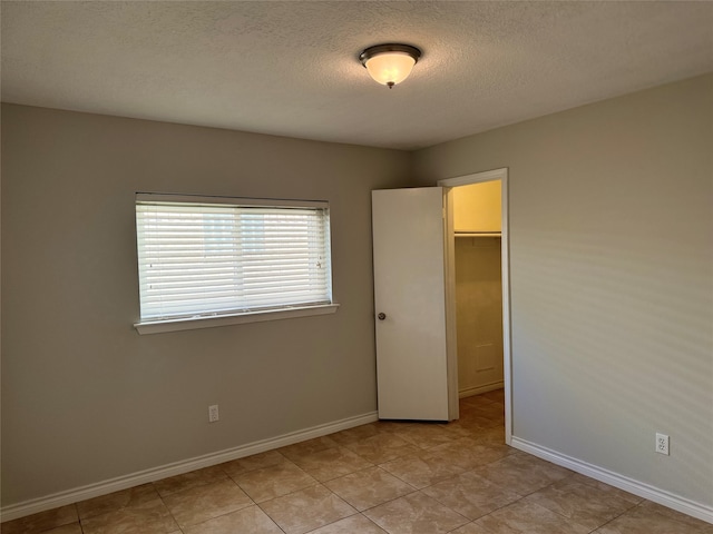 unfurnished bedroom featuring a walk in closet, a textured ceiling, light tile patterned floors, and a closet