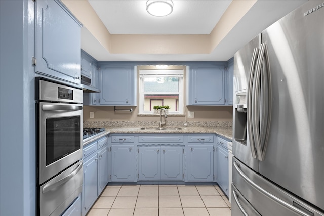 kitchen featuring appliances with stainless steel finishes, blue cabinetry, sink, and light tile patterned floors