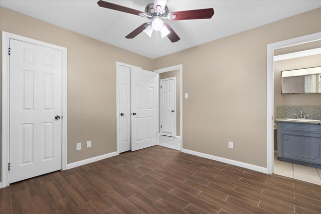 unfurnished bedroom featuring ensuite bath, sink, dark wood-type flooring, and ceiling fan