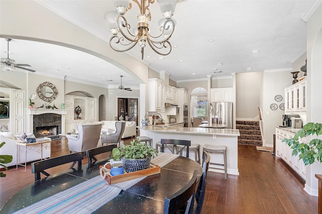 dining space with ceiling fan with notable chandelier, a premium fireplace, ornamental molding, and dark wood-type flooring