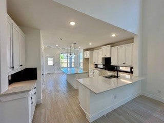 kitchen with pendant lighting, white cabinetry, sink, kitchen peninsula, and light hardwood / wood-style flooring