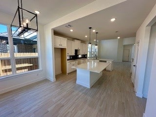 kitchen with hanging light fixtures, light hardwood / wood-style floors, a center island, and white cabinets