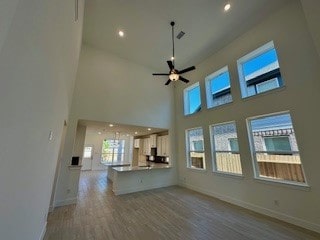 unfurnished living room with a towering ceiling, ceiling fan, and hardwood / wood-style flooring