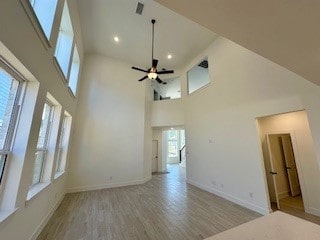 unfurnished living room with ceiling fan, light hardwood / wood-style floors, and a high ceiling