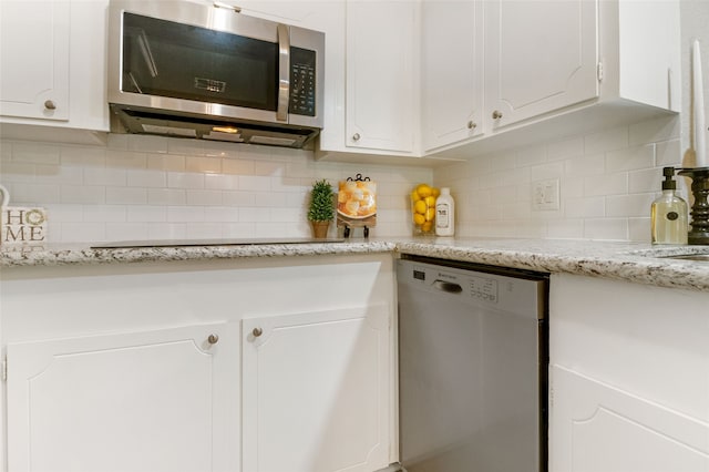 kitchen with appliances with stainless steel finishes, white cabinets, light stone counters, and backsplash