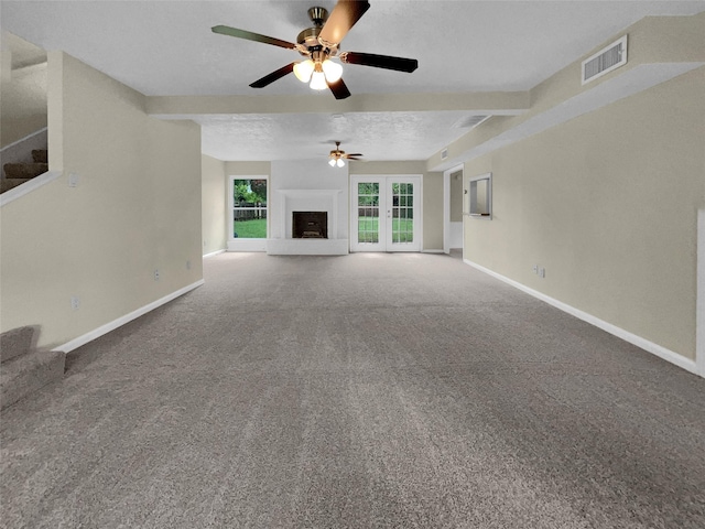 unfurnished living room featuring visible vents, a fireplace with raised hearth, a textured ceiling, carpet, and baseboards