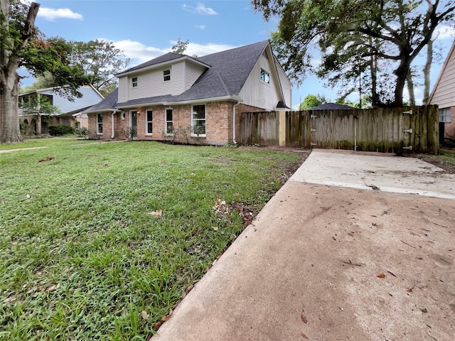 view of front of house with brick siding, roof with shingles, a front yard, and fence