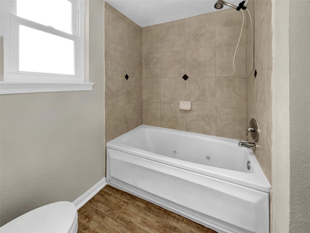 bathroom with toilet, wood finished floors, shower / washtub combination, baseboards, and a textured wall