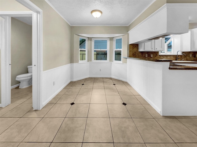 kitchen featuring light tile patterned flooring, white cabinets, crown molding, a textured ceiling, and dark countertops