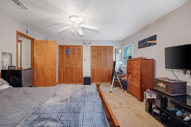 bedroom featuring carpet, two closets, a textured ceiling, and ceiling fan