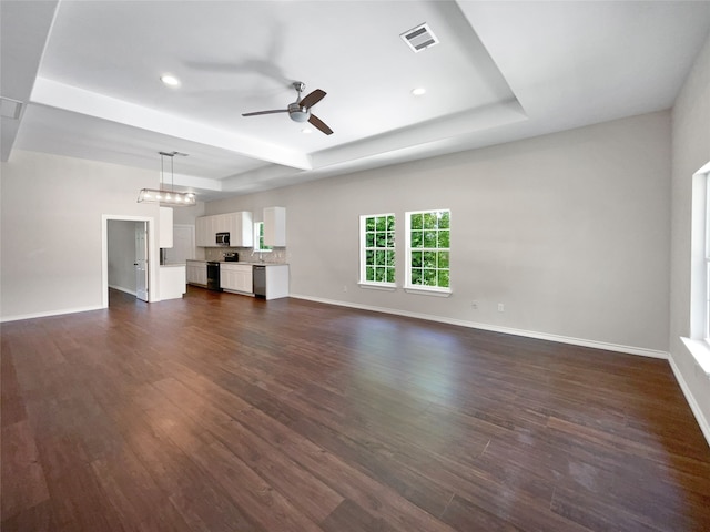 unfurnished living room featuring ceiling fan with notable chandelier, dark hardwood / wood-style flooring, and a tray ceiling