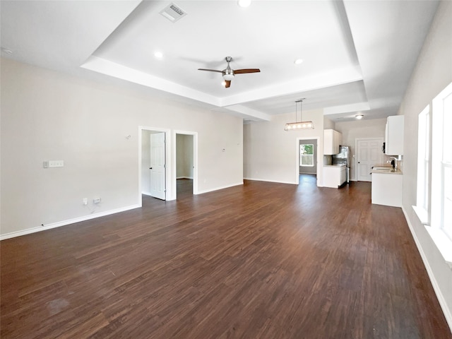 unfurnished living room featuring sink, dark hardwood / wood-style flooring, ceiling fan, and a tray ceiling