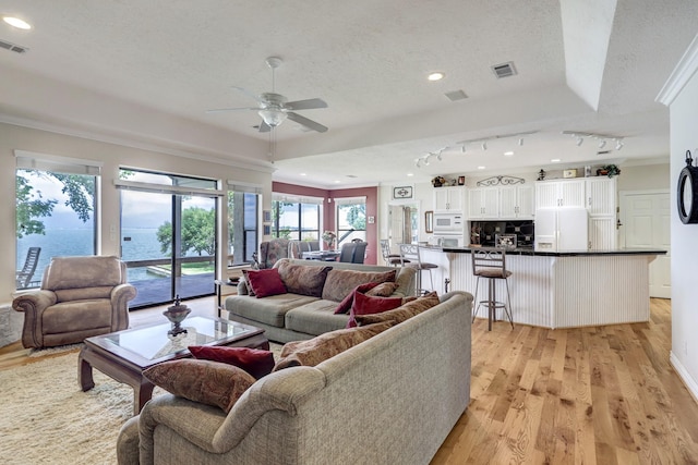 living room featuring ceiling fan, crown molding, light hardwood / wood-style floors, and a textured ceiling