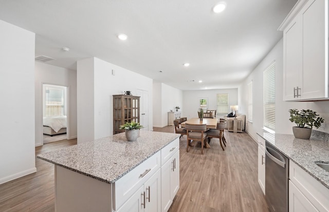 kitchen with white cabinets, a center island, stainless steel dishwasher, and light stone counters