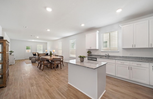 kitchen with white cabinets, sink, a kitchen island, light hardwood / wood-style floors, and light stone counters