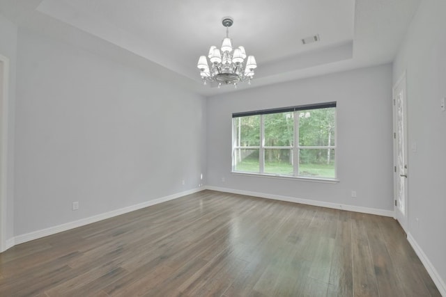 spare room featuring dark hardwood / wood-style flooring, a chandelier, and a raised ceiling