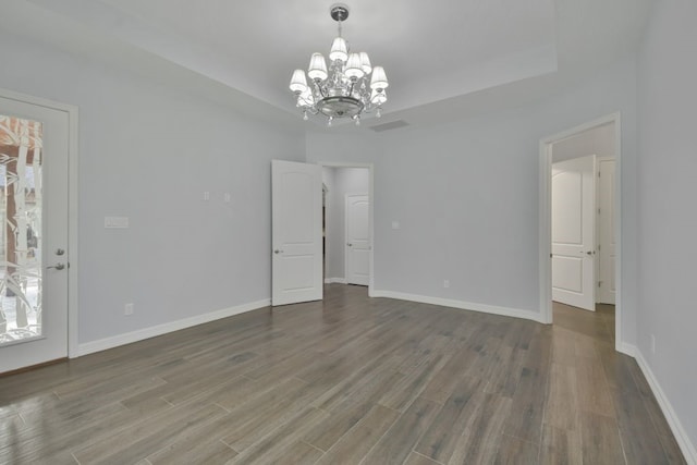 empty room featuring a chandelier, a raised ceiling, and hardwood / wood-style floors