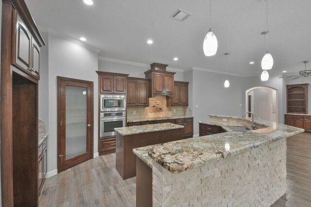 kitchen featuring stainless steel appliances, light stone counters, a large island with sink, sink, and tasteful backsplash