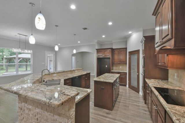 kitchen featuring tasteful backsplash, decorative light fixtures, black appliances, light stone counters, and a spacious island