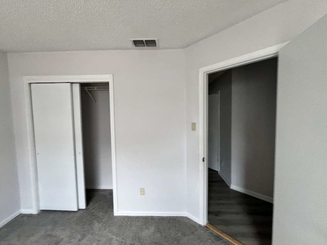 unfurnished bedroom featuring a closet, dark colored carpet, and a textured ceiling