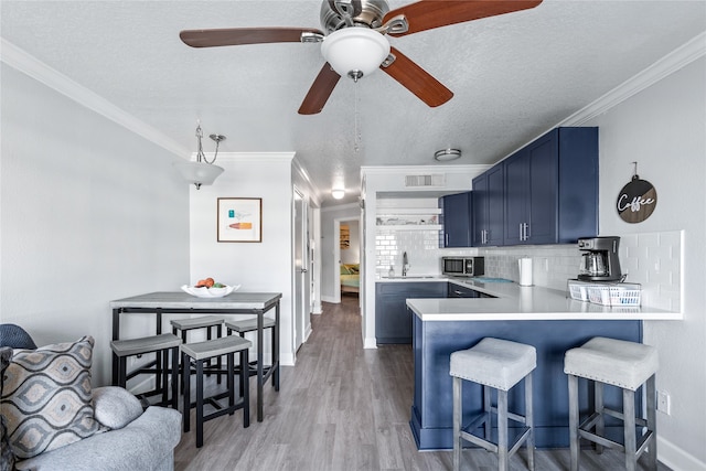 kitchen featuring ceiling fan, kitchen peninsula, tasteful backsplash, blue cabinets, and hardwood / wood-style flooring