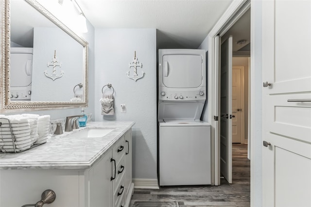 washroom with stacked washer and dryer, laundry area, wood finished floors, a sink, and baseboards