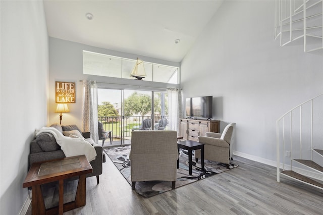 living area featuring baseboards, stairs, high vaulted ceiling, and wood finished floors