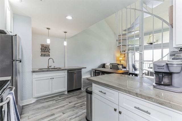 kitchen featuring light wood-style flooring, a peninsula, a sink, white cabinets, and appliances with stainless steel finishes