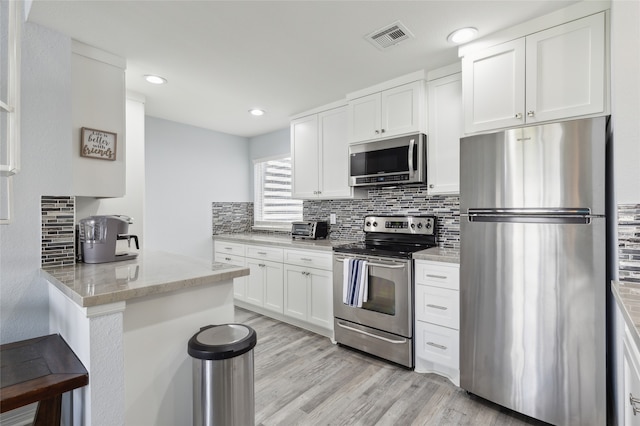 kitchen with stainless steel appliances, kitchen peninsula, light wood-type flooring, and white cabinetry