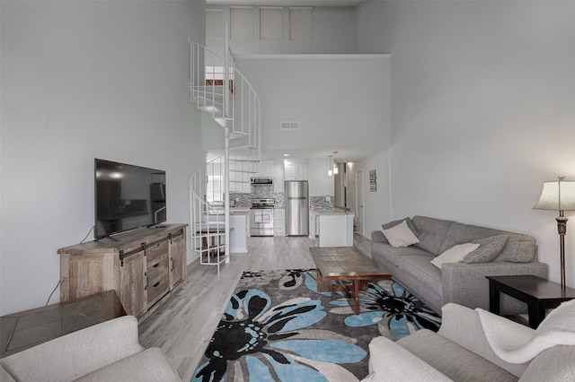 living room with stairway, light wood-type flooring, a towering ceiling, and visible vents