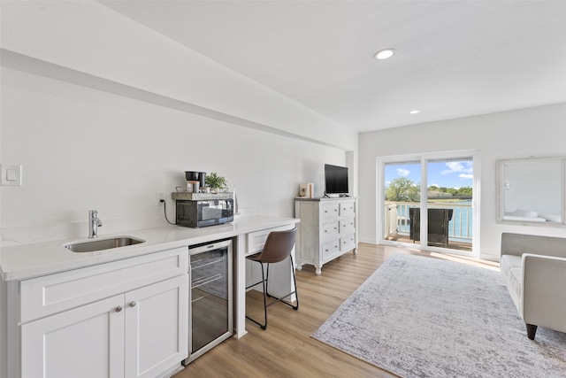 interior space with wine cooler, white cabinetry, light hardwood / wood-style flooring, sink, and a kitchen bar