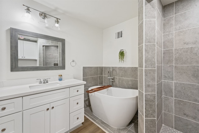 bathroom with tile walls, a bathtub, vanity, and wood-type flooring