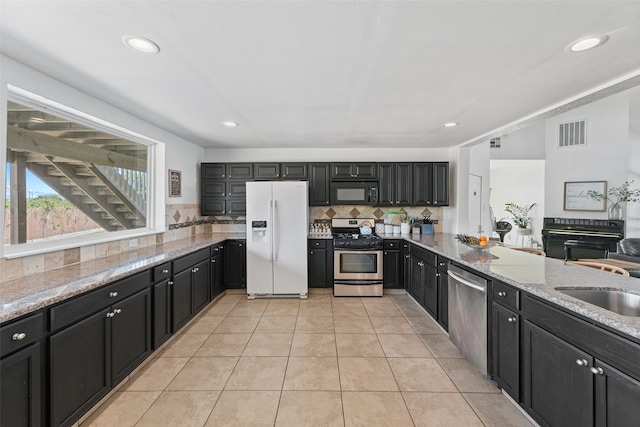 kitchen featuring stainless steel appliances, light tile patterned floors, light stone countertops, sink, and backsplash