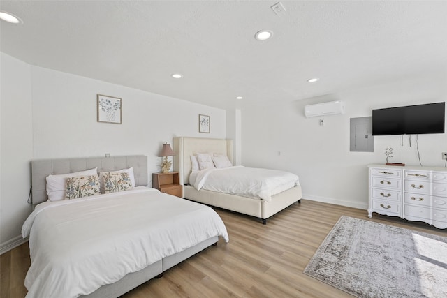 bedroom with an AC wall unit, light hardwood / wood-style flooring, and electric panel