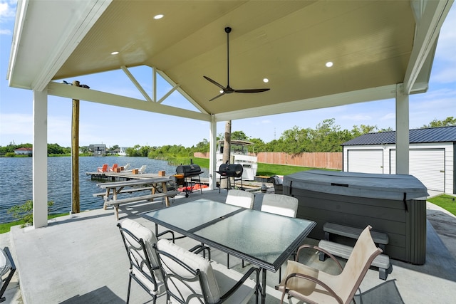 view of patio with an outbuilding, a water view, a boat dock, ceiling fan, and a hot tub