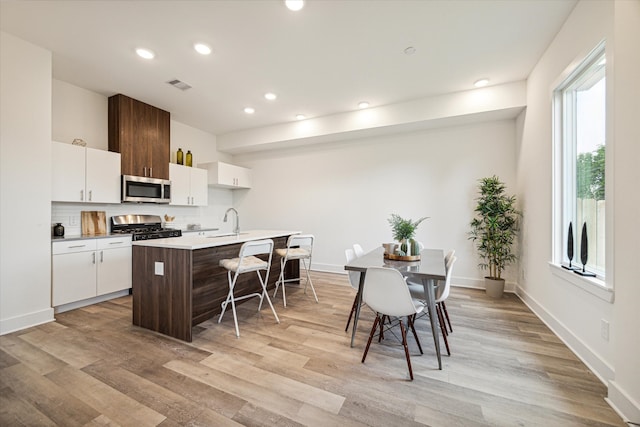 kitchen featuring light hardwood / wood-style flooring, stove, tasteful backsplash, an island with sink, and white cabinets