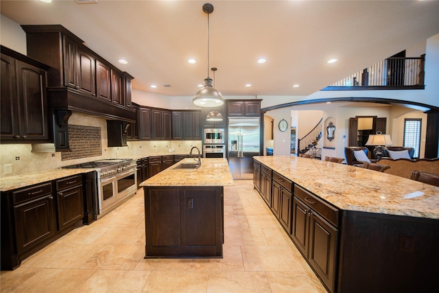 kitchen featuring dark brown cabinets, a spacious island, sink, built in appliances, and hanging light fixtures