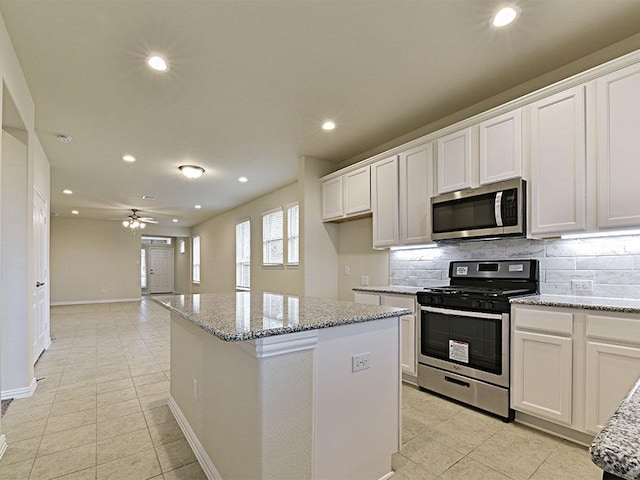 kitchen featuring light stone counters, stainless steel appliances, a kitchen island, and white cabinets