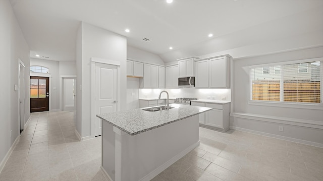 kitchen with light stone countertops, sink, an island with sink, light tile patterned floors, and appliances with stainless steel finishes