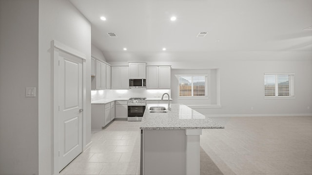 kitchen featuring appliances with stainless steel finishes, light stone counters, sink, light tile patterned floors, and an island with sink