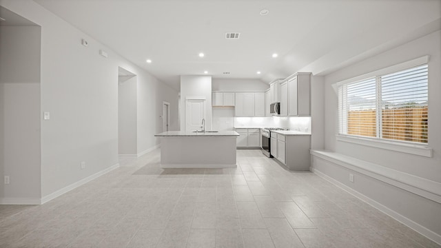 kitchen with backsplash, a kitchen island with sink, sink, appliances with stainless steel finishes, and light stone counters