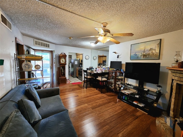 living room with ceiling fan, a textured ceiling, hardwood / wood-style flooring, and a brick fireplace