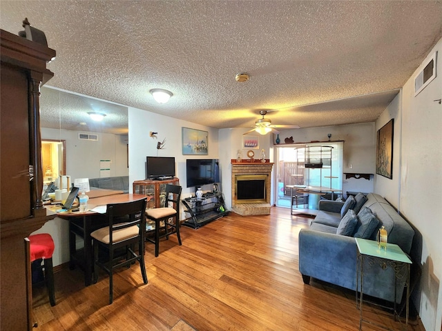 living room featuring ceiling fan, visible vents, a fireplace with raised hearth, and wood finished floors