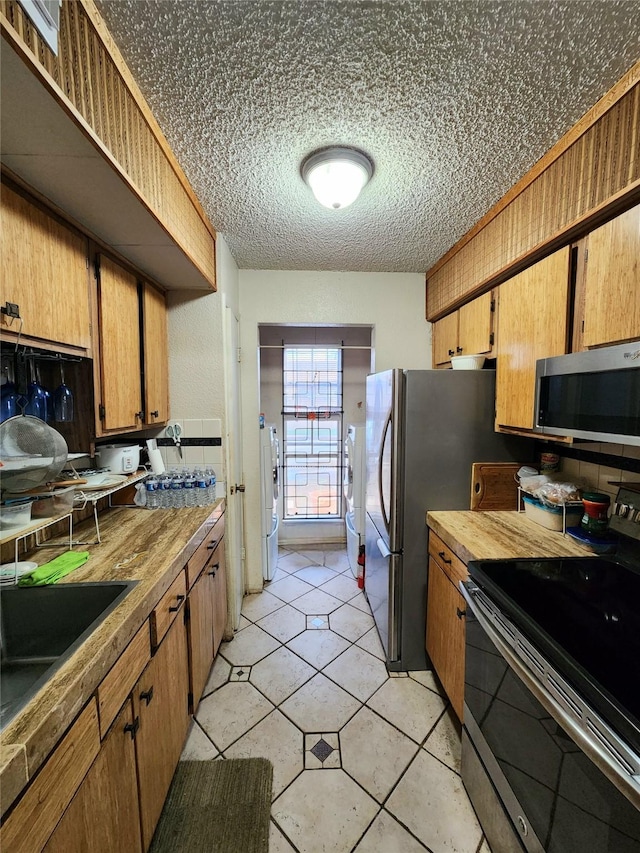 kitchen featuring washer / clothes dryer, brown cabinets, stainless steel appliances, a textured ceiling, and a sink