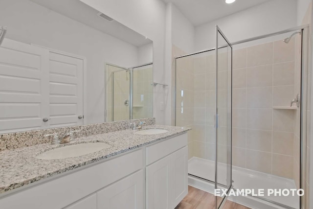 bathroom with dual bowl vanity, hardwood / wood-style floors, and a shower with shower door